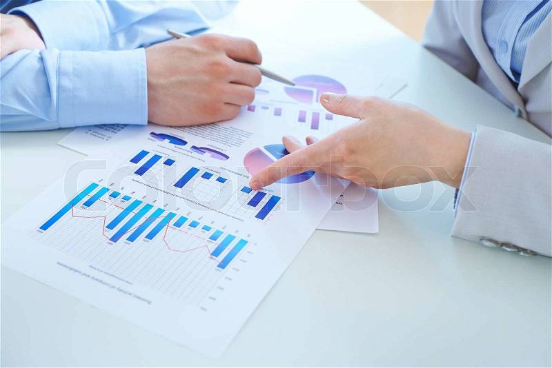 Close-up of female hand pointing at charts in business document during her report, stock photo