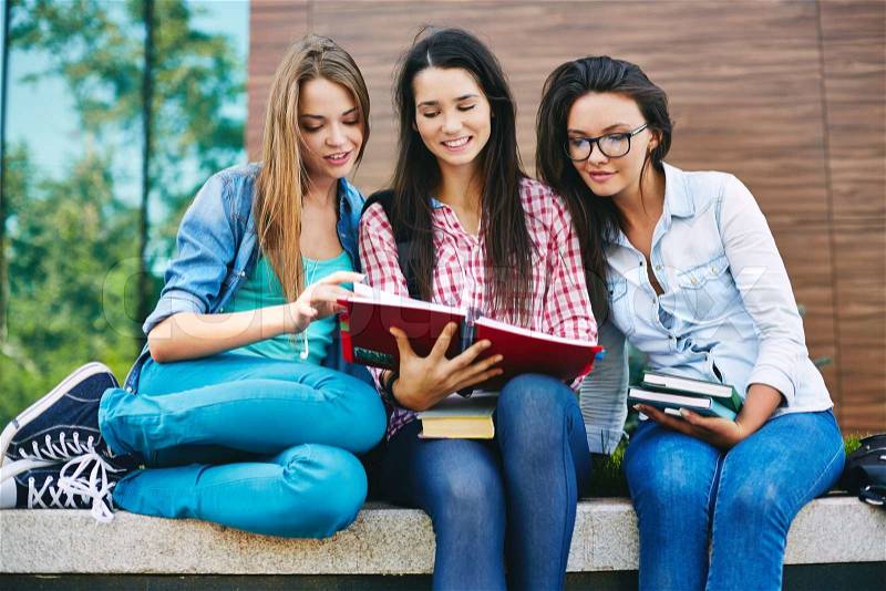 Company of happy teen girls reading book outside, stock photo