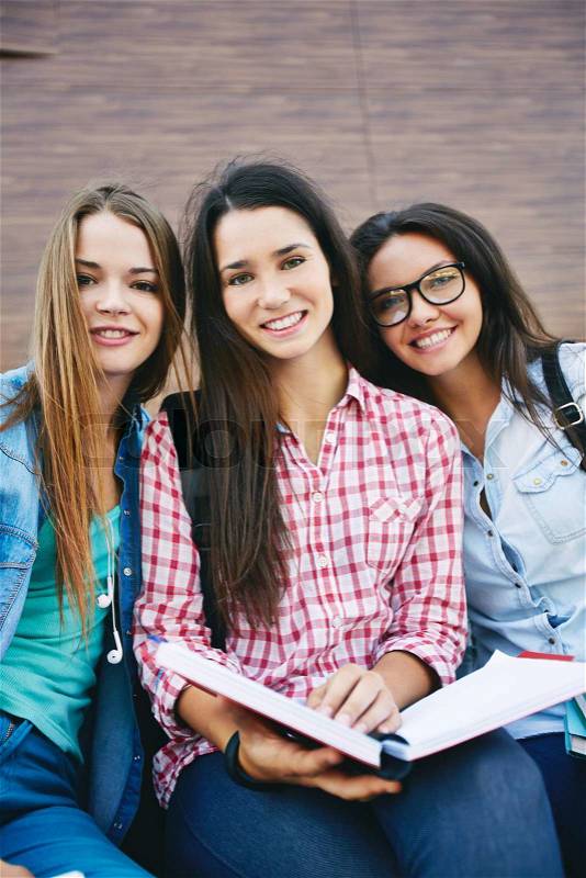 Company of happy teen girls with open book looking at camera outside, stock photo