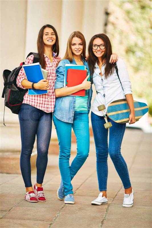Company of happy teen girls looking at camera white standing near college, stock photo