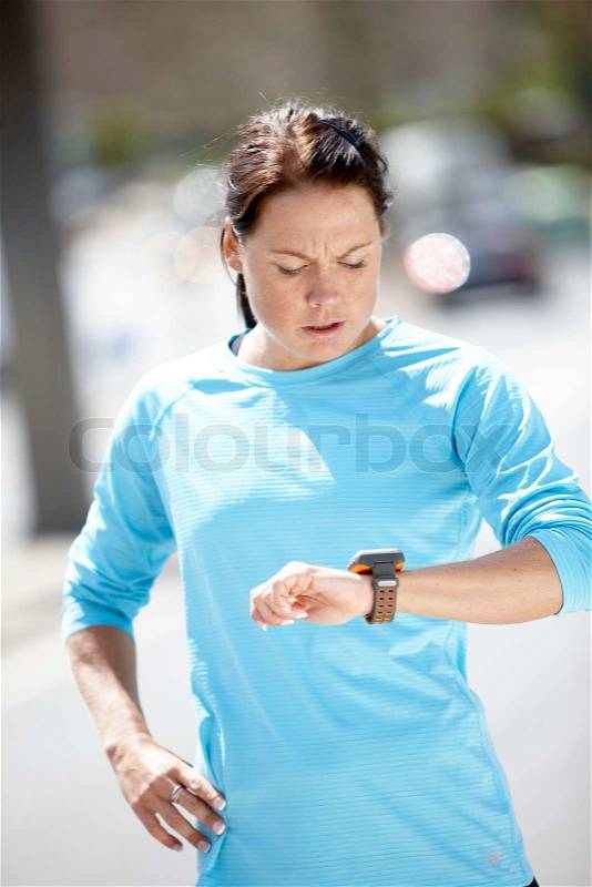 A young brunette caucasian woman in blue sportswear running and checking the time, stock photo
