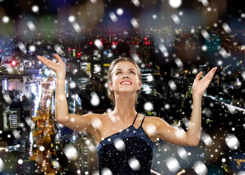 People, happiness, holidays and christmas concept - smiling woman raising hands and looking up over snowy night city background, stock photo