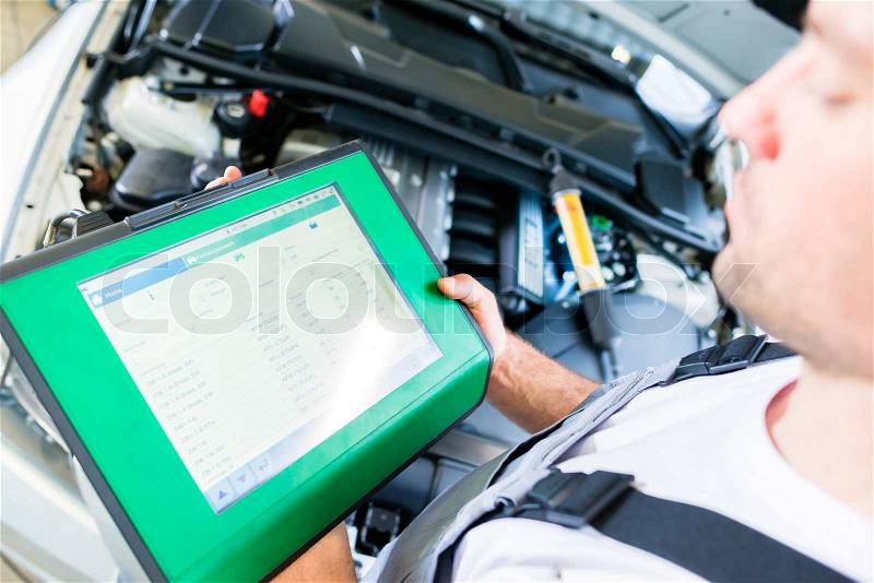 Mechanic with diagnostic tool in car workshop, stock photo