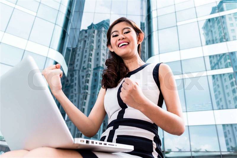 Asian businesswoman working on laptop in front of tower building, stock photo