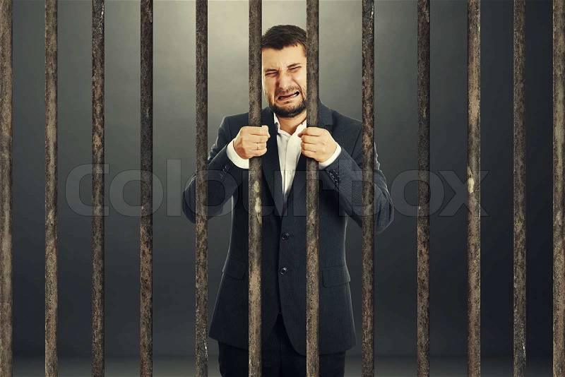 Crying businessman behind the prison cell over dark background, stock photo