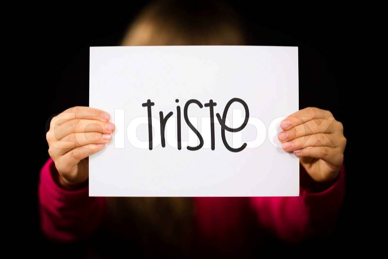 Studio shot of child holding a sign with Spanish word Triste - Sorry, stock photo