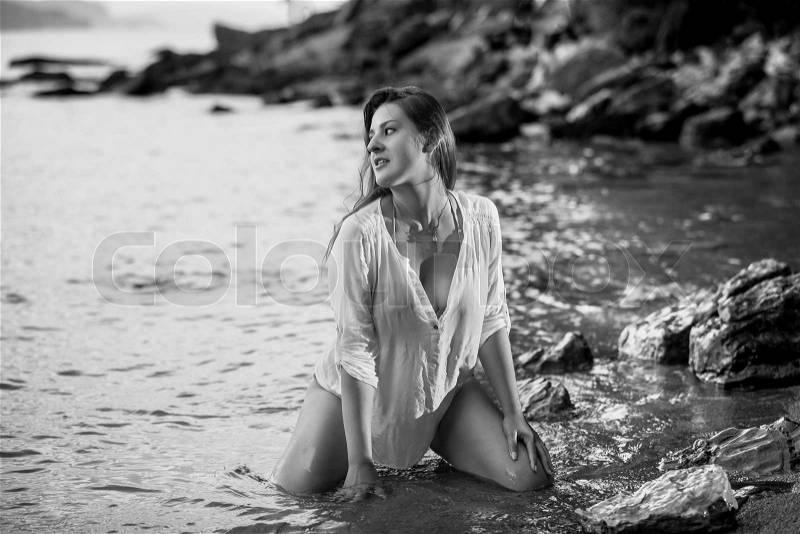 Black and white photo of sexy young woman kneeling at sea shore, stock photo