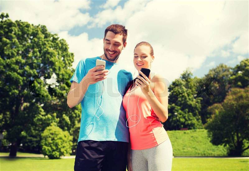 Fitness, sport, training, technology and lifestyle concept - two smiling people with smartphones and earphones outdoors, stock photo