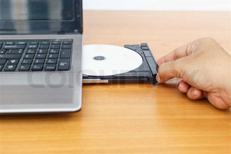 Hand inserting a cd on laptop on table, stock photo