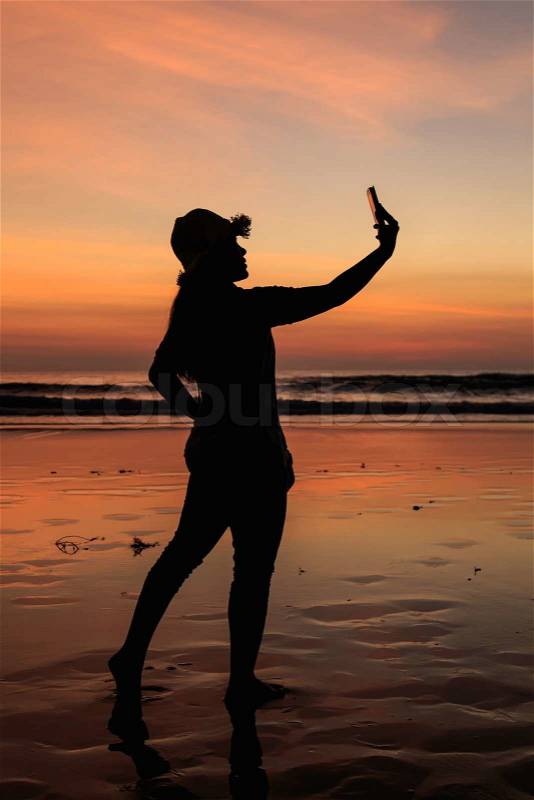 Silhouette of Thai Woman using smartphone at the beach in sunset time, stock photo