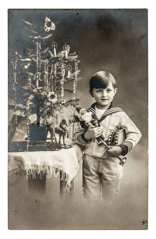 Stock image of 'happy boy with christmas tree, gifts and vintage toys. antique sepia picture with original film grain and scratches'
