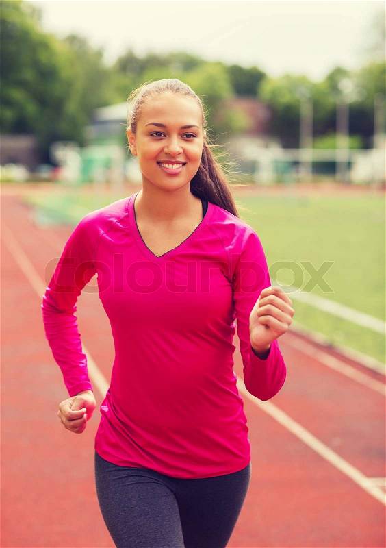 Fitness, sport, training and lifestyle concept - smiling african american woman running on track outdoors, stock photo