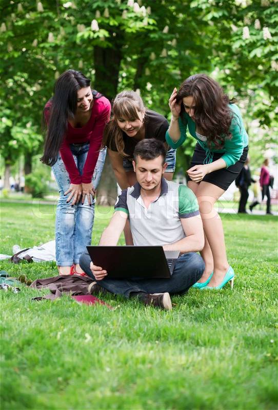 Group of young college students sitting on grass in the park, stock photo