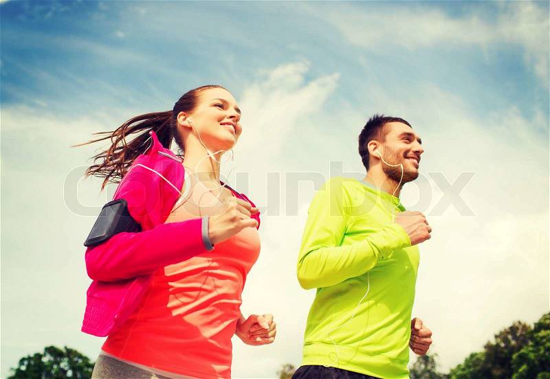 Fitness, sport, friendship and lifestyle concept - smiling couple with earphones running outdoors, stock photo