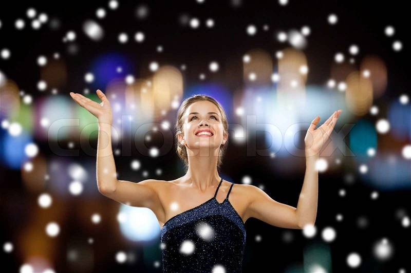 People, happiness, holidays and christmas concept - smiling woman raising hands and looking up over snowy night city lights background, stock photo