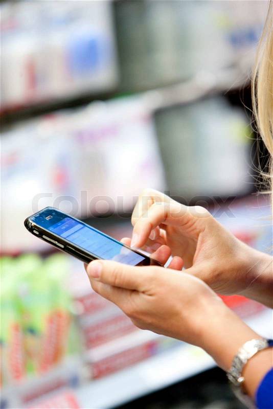 A young blond, caucasian woman in a supermarket checking her smartphone, stock photo
