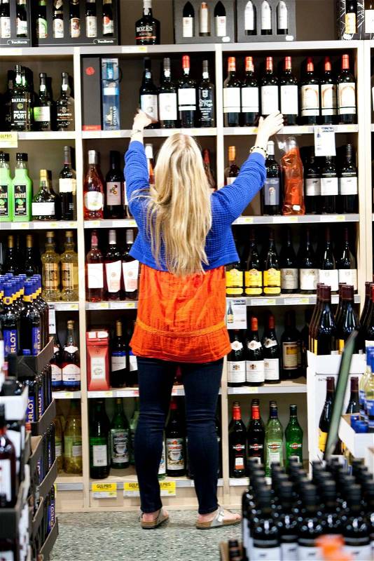 A young blond, caucasian woman in a supermarket buying wine, stock photo