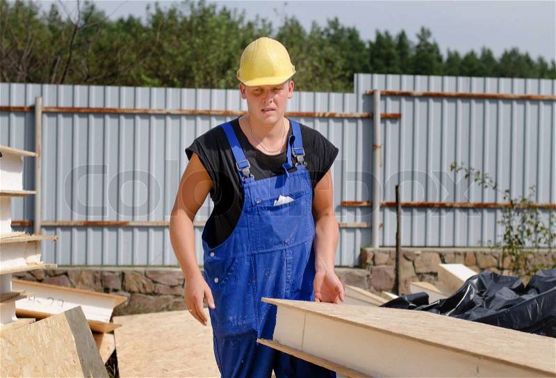 Builder carrying an insulated wooden wall panel on an outdoor bulding site which he has just selected from a pile of building material, stock photo