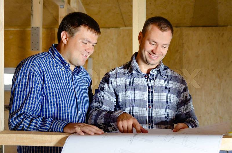 Two builders discussing a building plan as they stand in the interior of a new build timber frame house still under construction, stock photo
