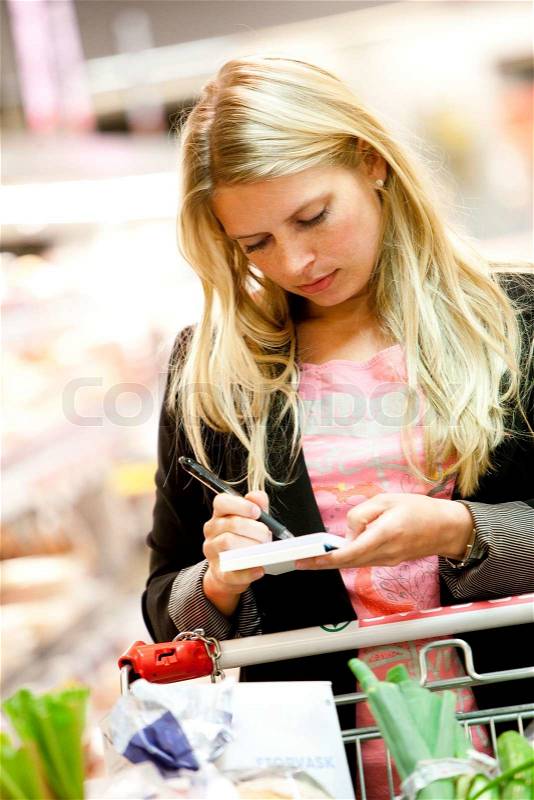 A young blond caucasian woman reading her grocery list while in a supermarket, stock photo