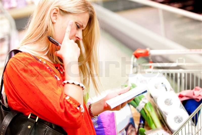 A young female blond caucasian reading a grocery list (stock photo), stock photo