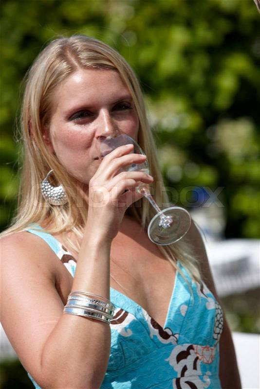 A young female European drinking white wine and enjoying a summer outdoors party, stock photo