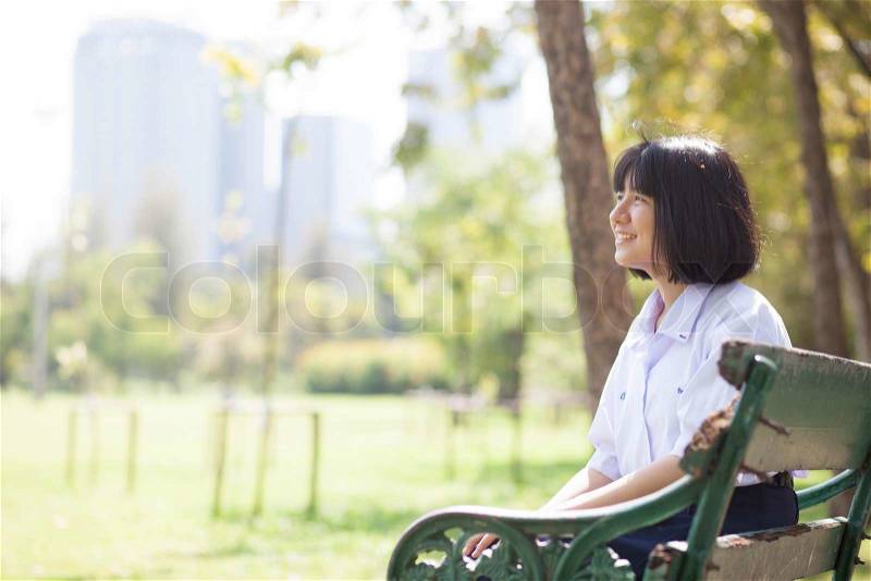 Schoolgirl sitting on the bench. Within the park. Girl smiling, stock photo