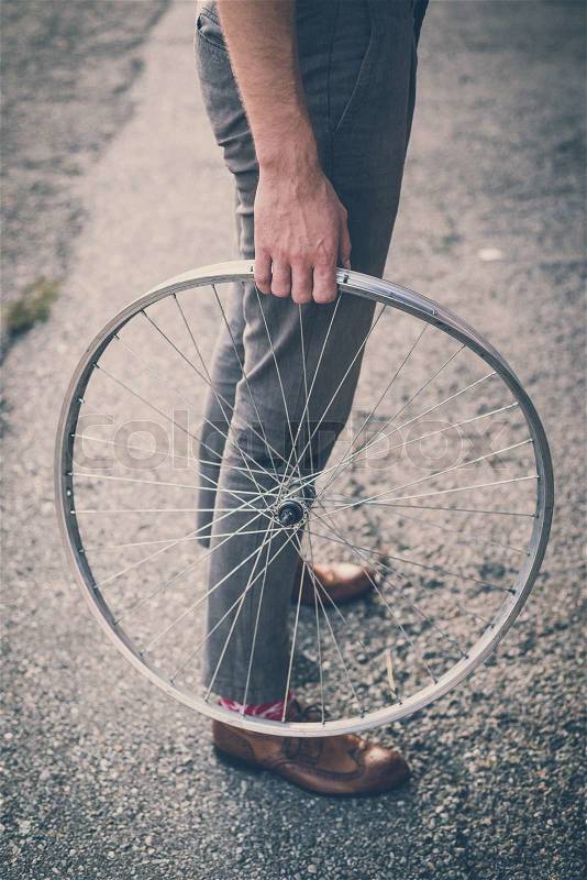 Close up of legs shoes hipster man holding old bicycle wheel in the city, stock photo