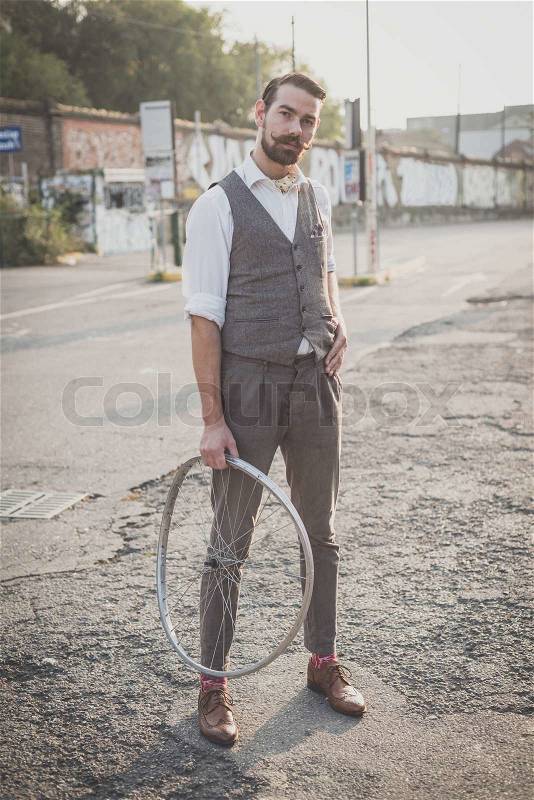 Handsome big moustache hipster man holding old bicycle wheel in the city, stock photo