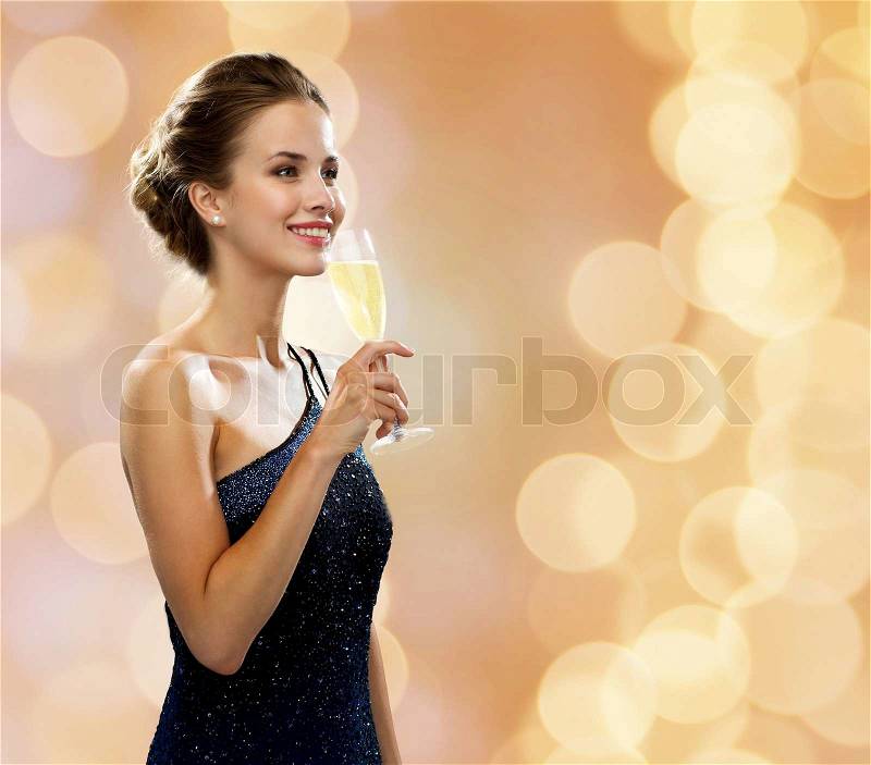 Party, drinks, holidays, people and celebration concept - smiling woman in evening dress with glass of sparkling wine over beige lights background, stock photo