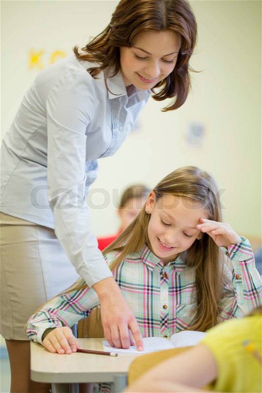 Education, elementary school, learning and people concept - teacher helping school girl writing test in classroom, stock photo
