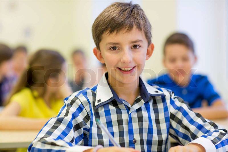 Education, elementary school, learning and people concept - group of school kids with pens and notebooks writing test in classroom, stock photo