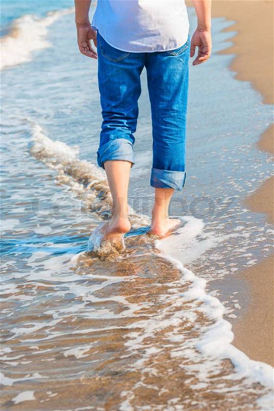 Barefoot man in jeans walking on the sea shore, stock photo