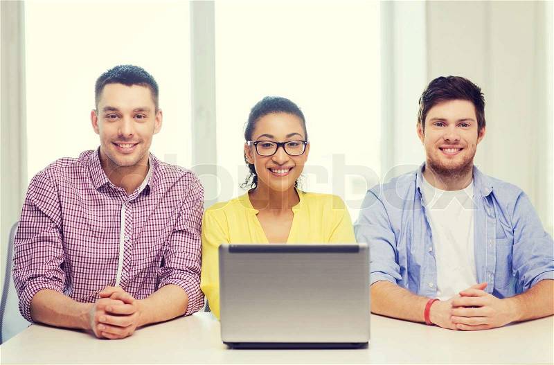Education, technology, business, startup and office concept - three smiling colleagues with laptop in office, stock photo