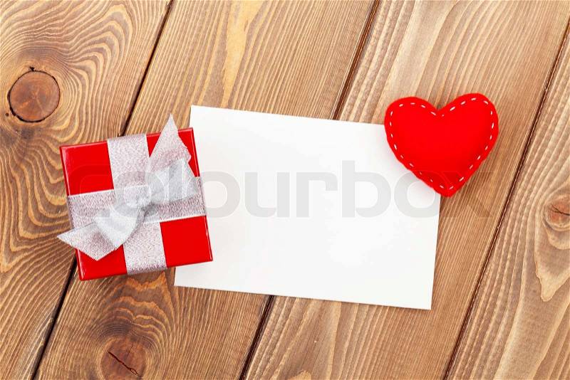 Photo frame or greeting card with gift box and toy heart over wooden table background, stock photo