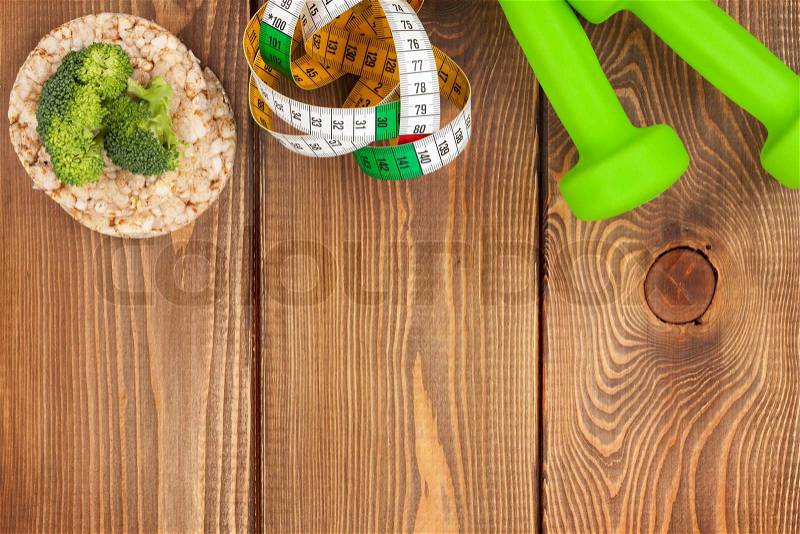 Dumbells, tape measure and healthy food over wooden table with copy space. Fitness and health, stock photo