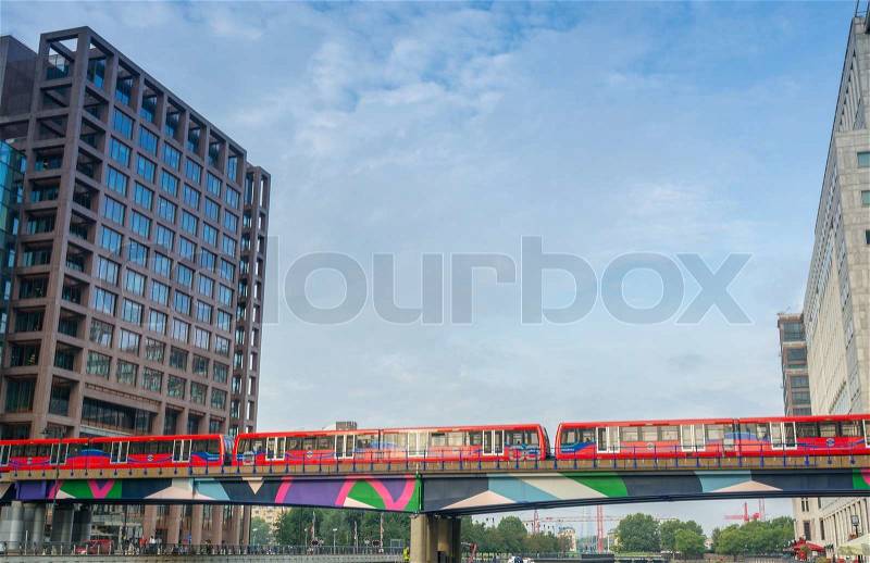 LONDON - AUG 20, 2013: Red train crosses river between Canary Wharf skyscrapers. Canary Wharf is a major business district located in Tower Hamlets, stock photo