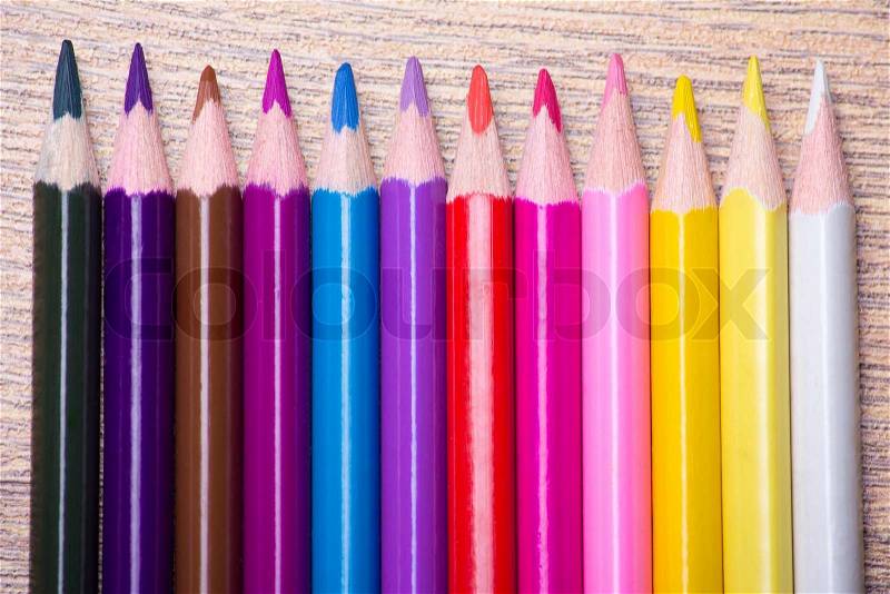 Row of many colored drawing pencils on wooden table background, stock photo