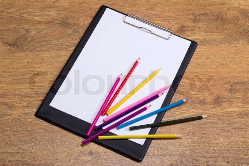 Colorful drawing pencils and clipboard with blank paper on wooden table background, stock photo