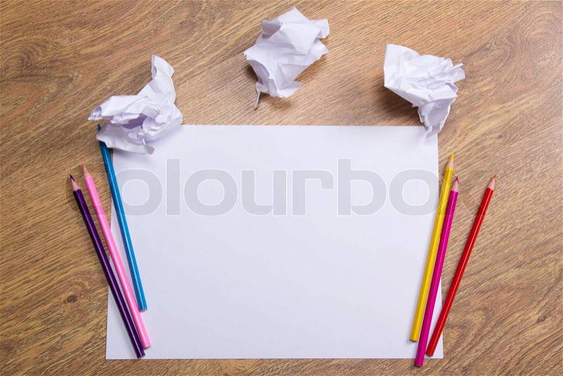 Colorful pencils on clear white paper with crumble paper balls on wooden table background, stock photo