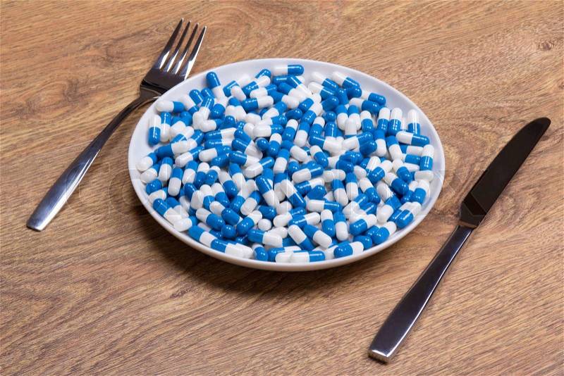 Diet concept - blue pills in plate with knife and fork on wooden table, stock photo