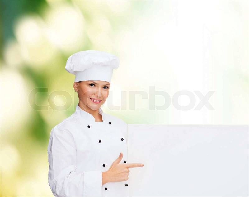 Cooking, advertisement and people concept - smiling female chef, cook or baker pointing finger to white blank board over green background, stock photo