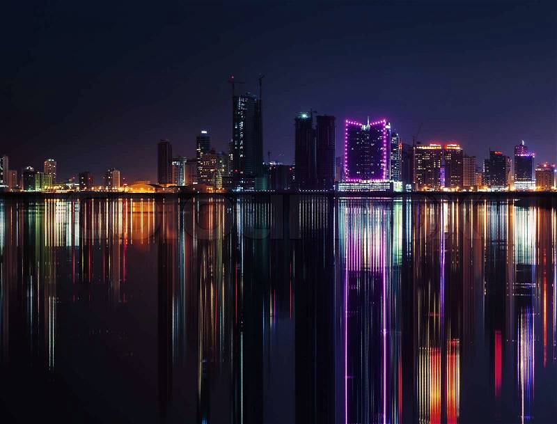 Night modern city skyline with shining neon lights and reflection in the water. Manama, the Capital of Bahrain, Middle East, stock photo