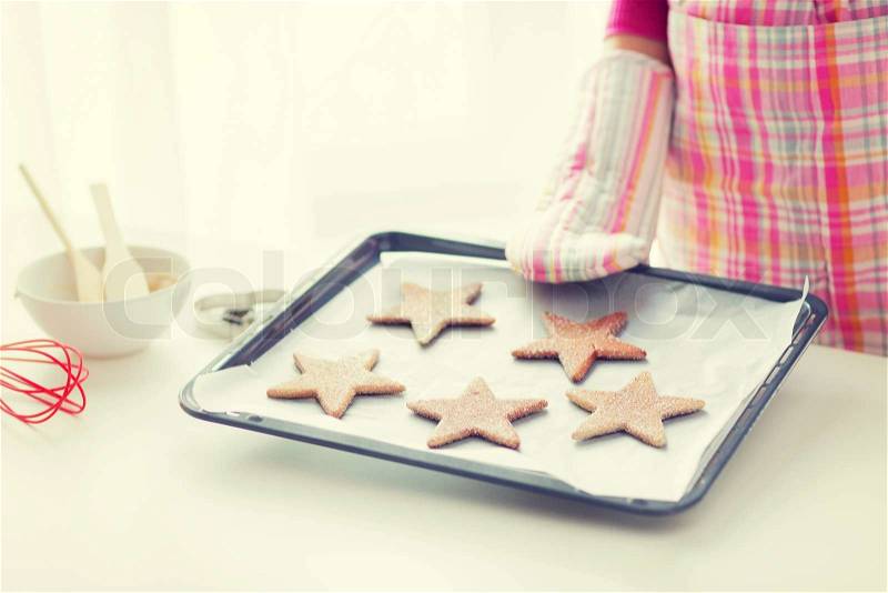 Christmas, food, holidays and people concept - close up of woman in apron and oven glove with cookies on oven tray, stock photo