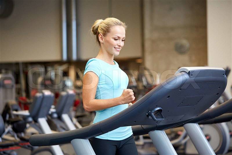 Sport, fitness, lifestyle, technology and people concept - smiling woman exercising on treadmill in gym, stock photo