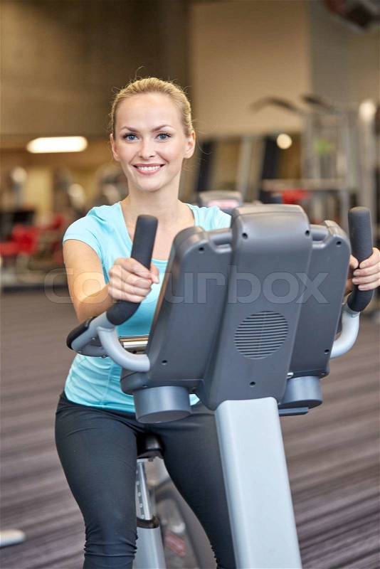 Sport, fitness, lifestyle, technology and people concept - smiling woman exercising on exercise bike in gym, stock photo