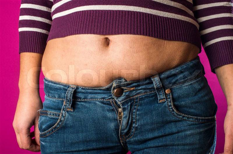 Woman with jeans shows her belly. Overweight, stock photo