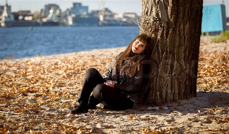 Beautiful woman sitting under tree on beach at sunny day, stock photo