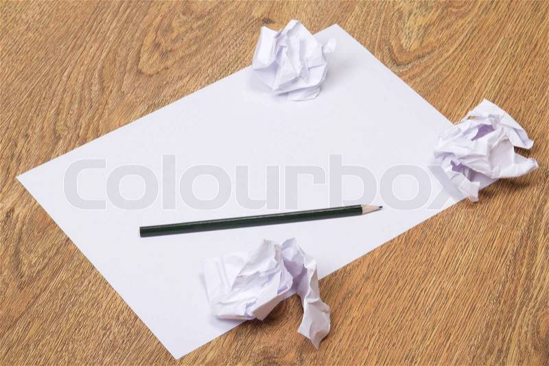 Black pencil on clear white paper with crumble paper balls on wooden table background, stock photo