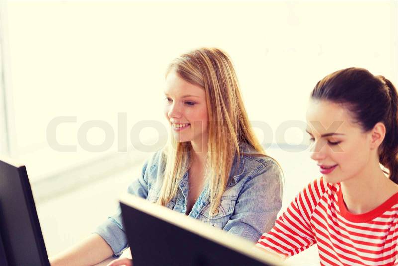 Education, technology and school concept - two smiling student girls in computer class, stock photo